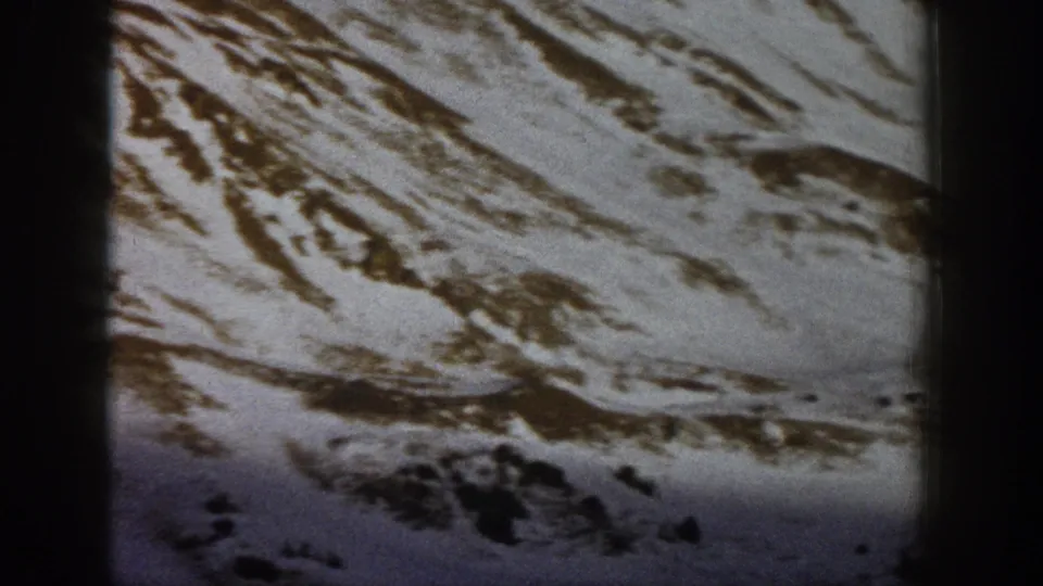 1961 Aspen-area 8mm frame showing a winter mountain slope with brown exposed patches and evergreen trees along the lower ridge.
