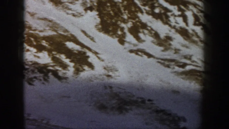 1961 Aspen-area home-movie frame of a snow-covered mountain face with dark foreground shadow and exposed brown terrain bands.