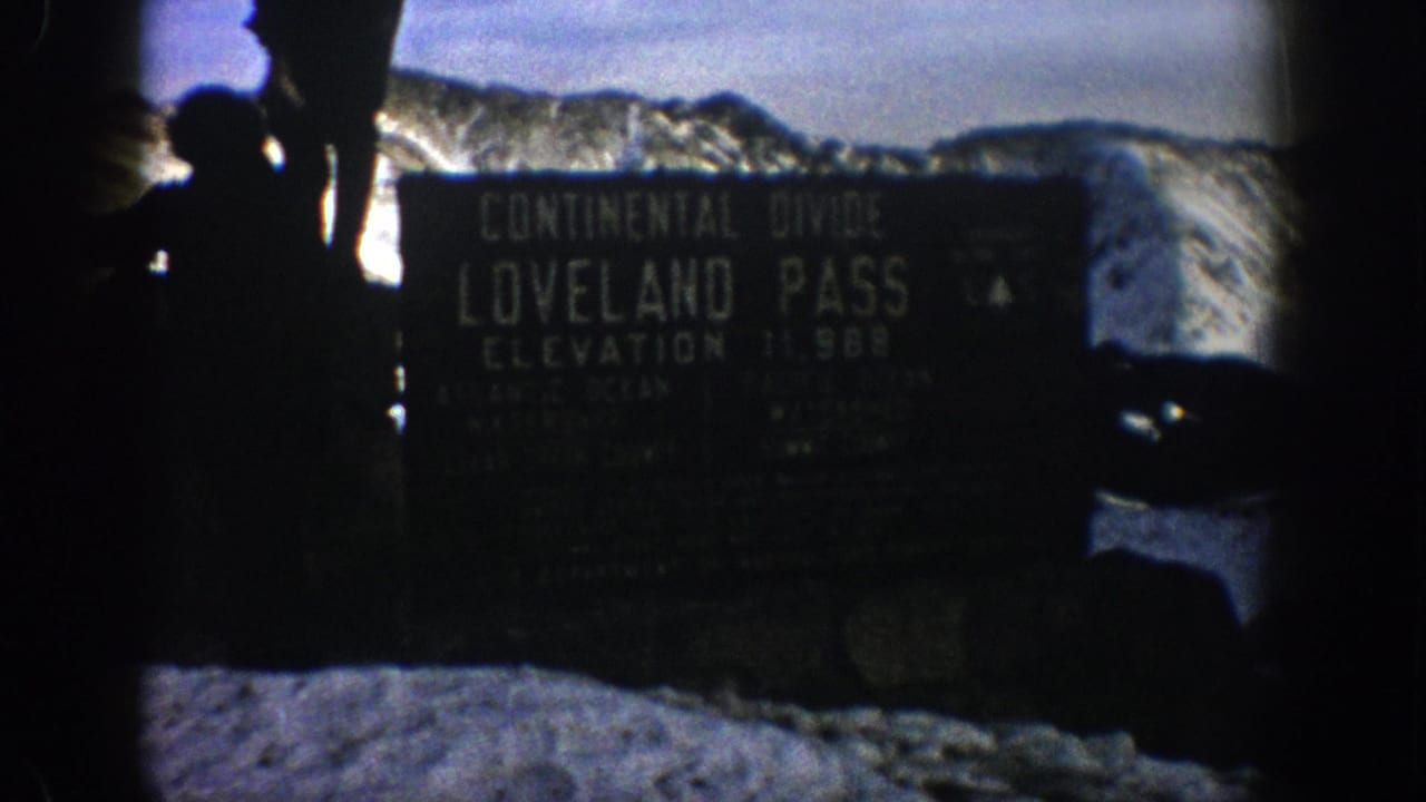 Silhouetted people beside a Loveland Pass Continental Divide sign in snow.