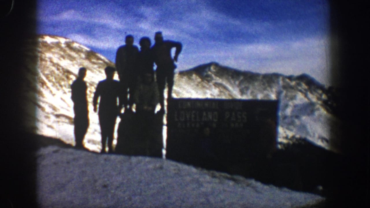 1961 8mm Colorado travel footage shows men silhouetted beside the Loveland Pass Continental Divide sign on a snowy mountain summit.