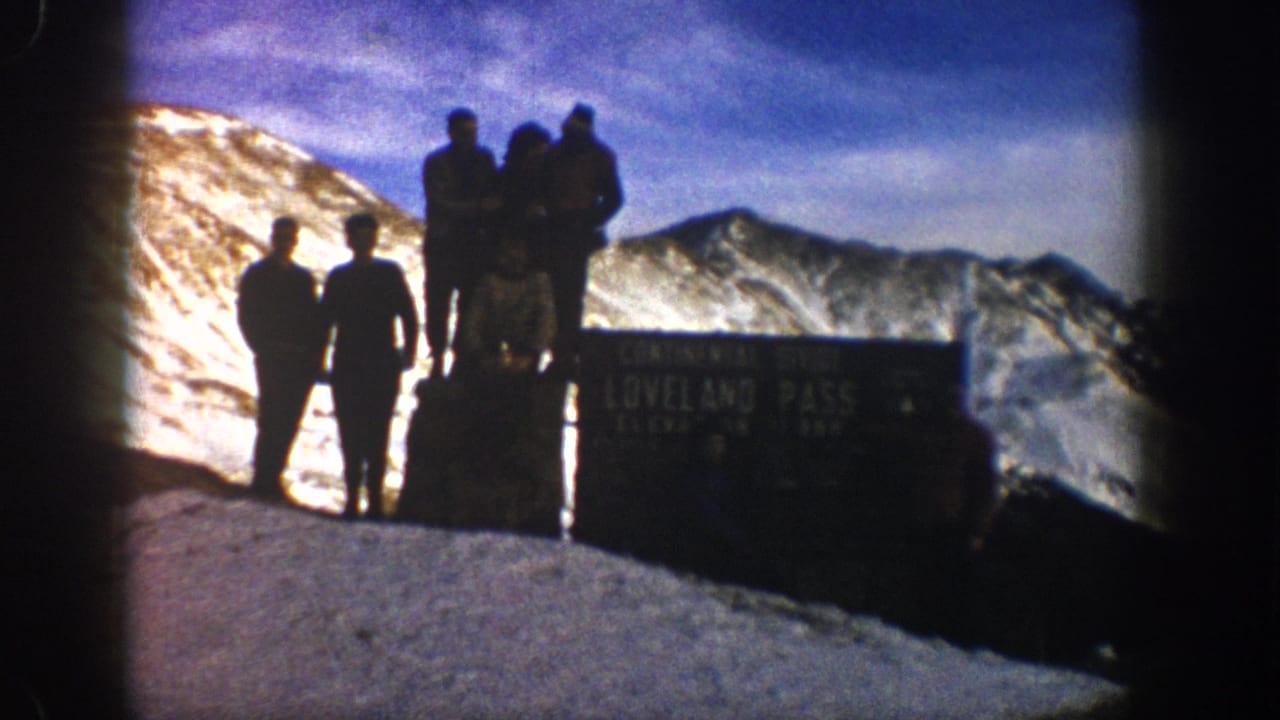 A group of hikers poses on and beside a Loveland Pass sign in bright mountain light.