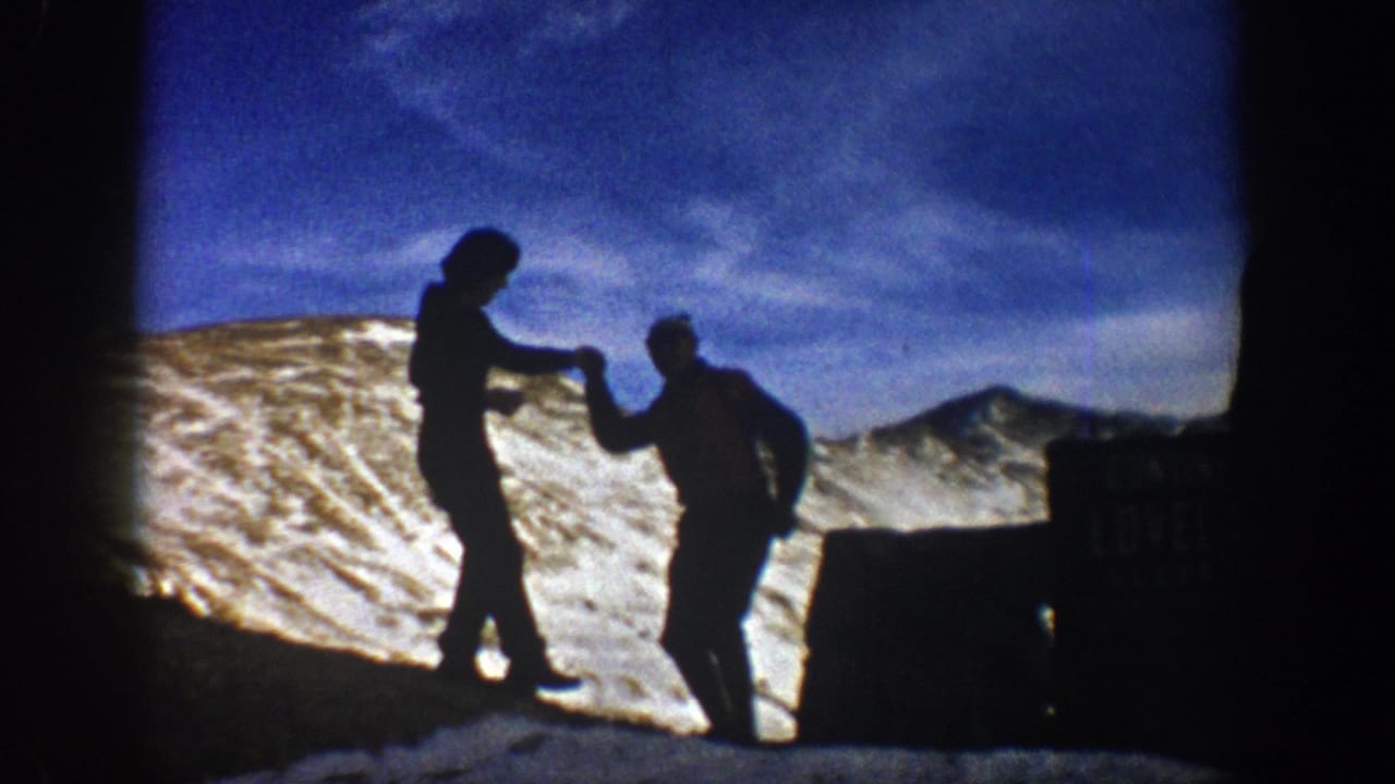 At Loveland Pass, one silhouetted hiker appears to handle a camera while another poses near the snowy roadside sign.