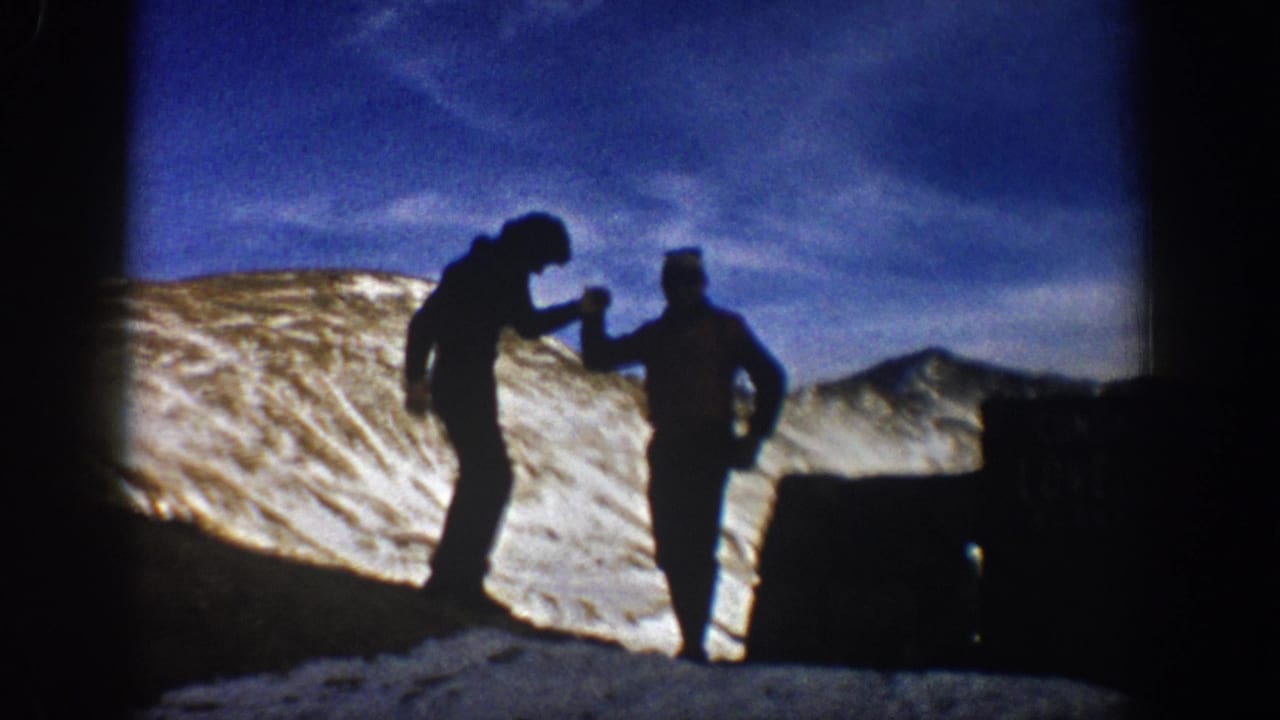 Two hikers in silhouette share a candid moment at Loveland Pass, framed by snow, blue sky, and a roadside sign.