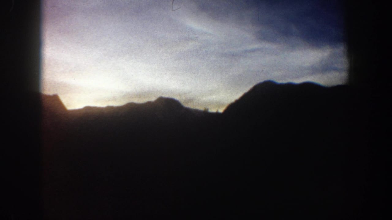 Dark mountain ridge silhouette against a warm golden-yellow glowing horizon; Aspen, Colorado area, circa 1961, 8mm home movie footage.