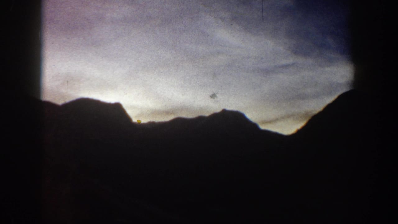 Mountain peaks in silhouette with sky transitioning from warm to cool tones; 8mm home movie circa 1961, Aspen, Colorado area.