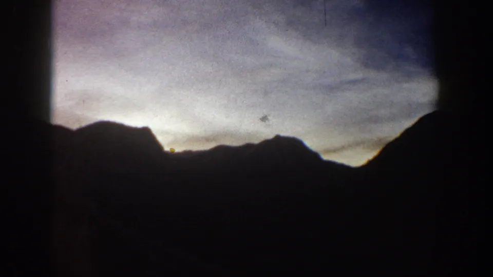 Mountain peaks in silhouette with sky transitioning from warm to cool tones; 8mm home movie circa 1961, Aspen, Colorado area.