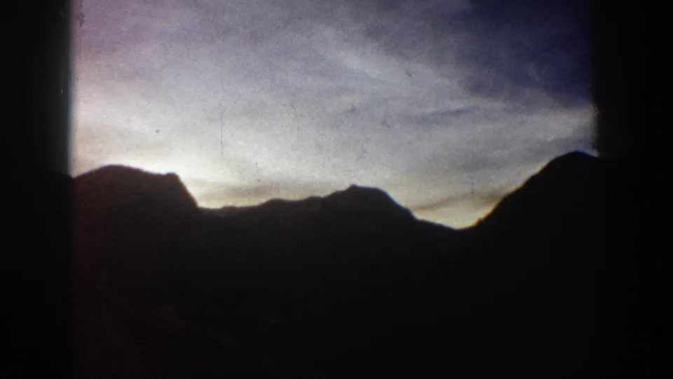 Rocky mountain ridge in silhouette against a purple-lavender twilight sky; 8mm home movie circa 1961, Aspen, Colorado area.