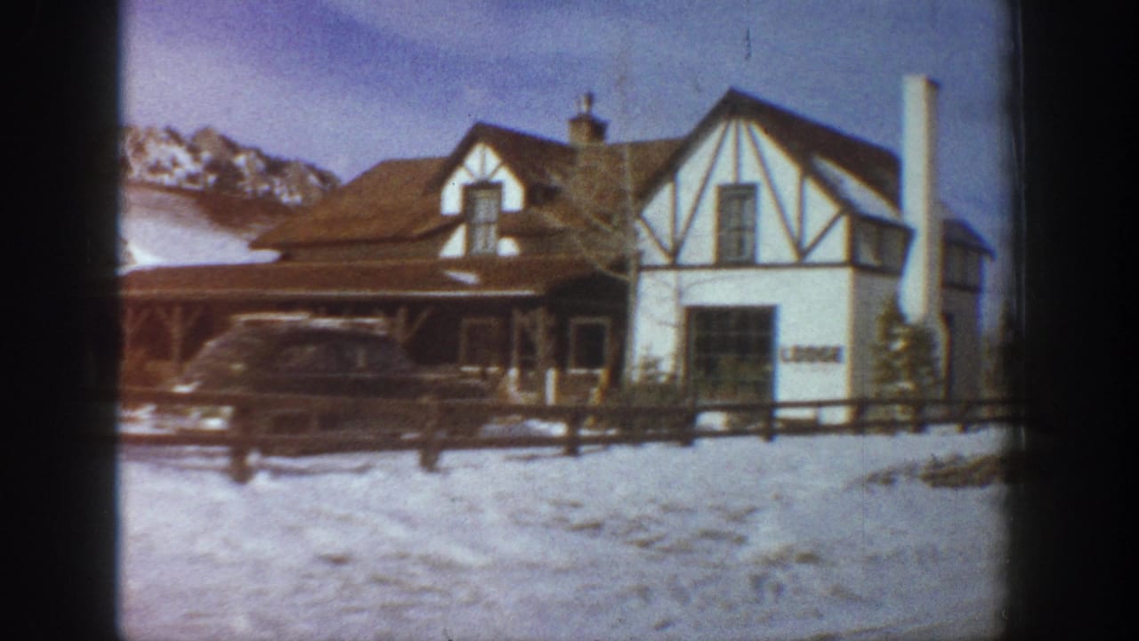 Tudor-revival alpine lodge with half-timber white facade, partial signage, snow-covered grounds and mountain range behind, Aspen Colorado area circa 1961.