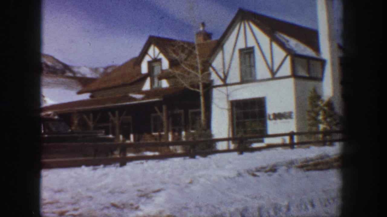 Tudor-revival lodge exterior in winter with partial building signage and mountain range behind, Aspen Colorado area circa 1961, shot on 8mm film.