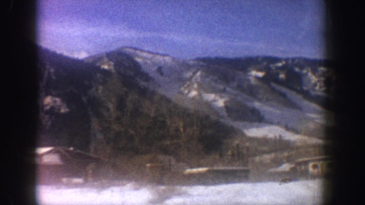 Pan across alpine valley with snow-patched mountain ridges and valley buildings under blue sky, Aspen Colorado area, circa 1961, 8mm film.