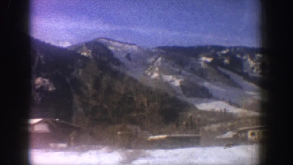Pan across alpine valley with snow-patched mountain ridges and valley buildings under blue sky, Aspen Colorado area, circa 1961, 8mm film.