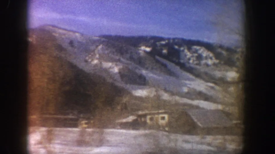 Continued camera pan across alpine valley with snow-covered slopes and structures at valley floor, Aspen Colorado area, circa 1961, 8mm.