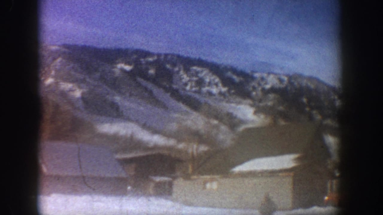 Blue-tinted 8mm frame showing a large flat-roofed building at the base of a heavily snow-covered mountain.