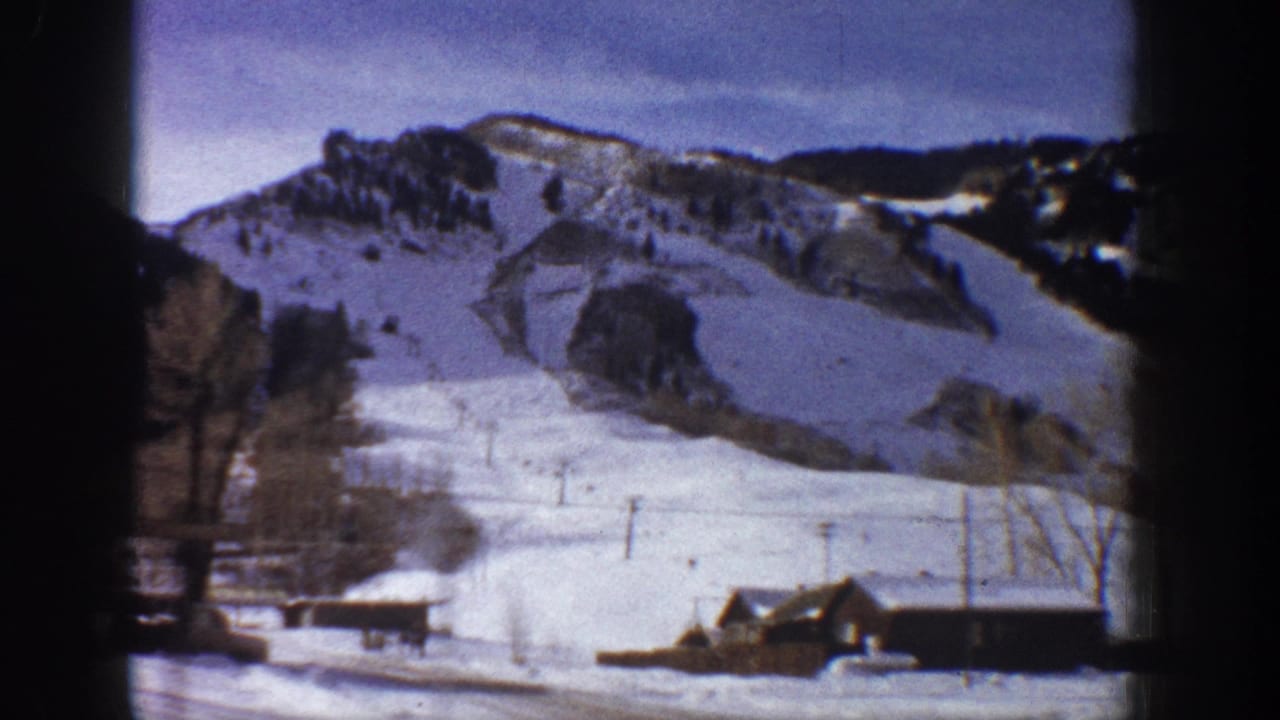Continuing 8mm pan over snow-covered Aspen valley with small buildings and bare trees under winter sky, circa 1961.