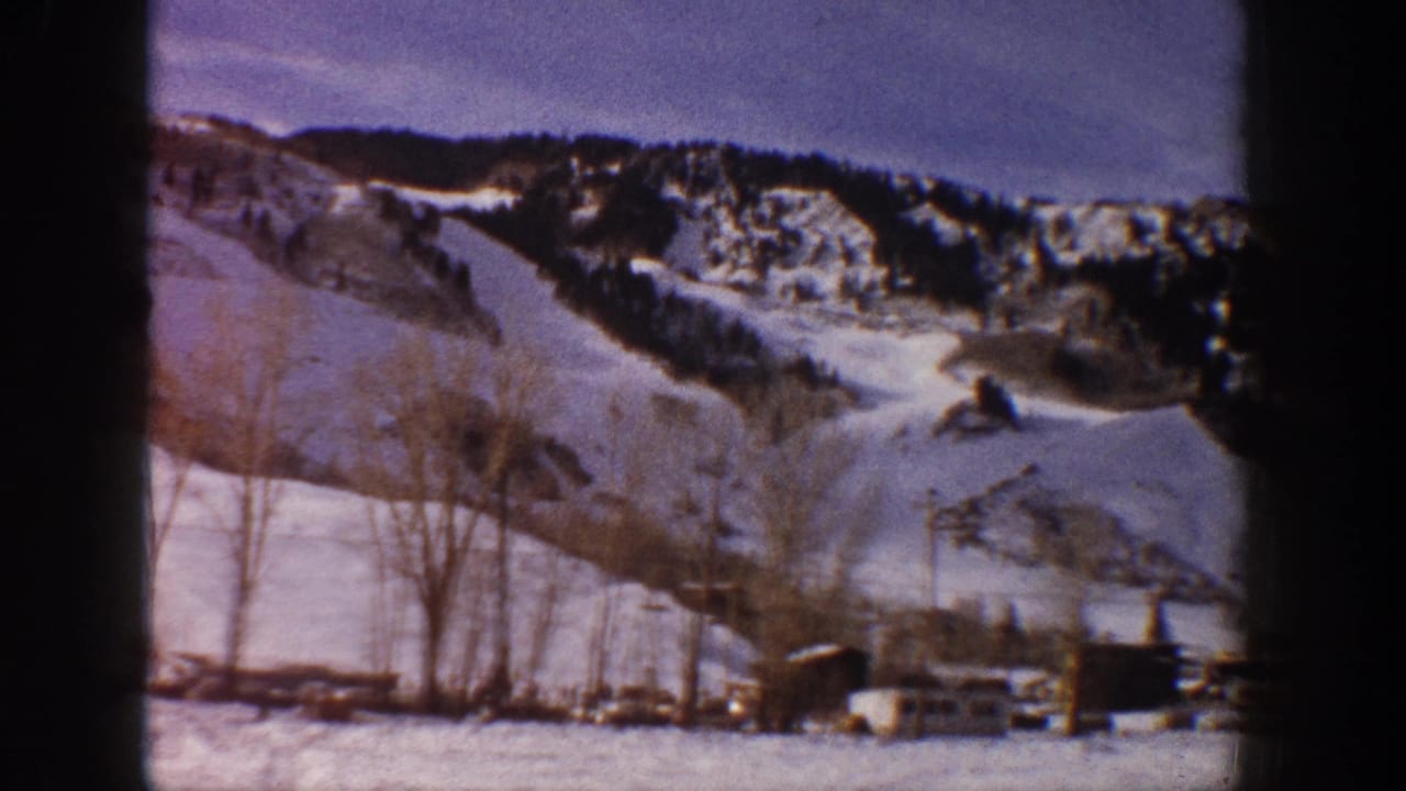 8mm home movie frame of a snow-covered Aspen hillside with scattered small structures, rocky outcroppings, and bare trees, c. 1961.