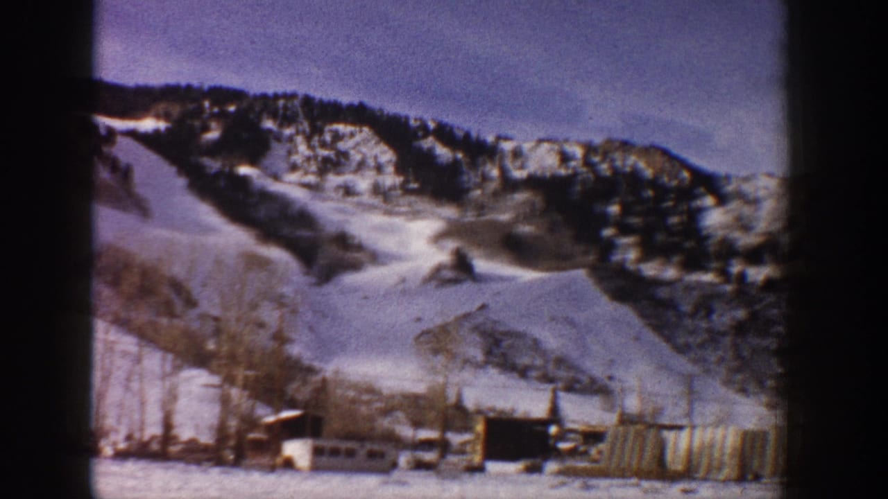 8mm home movie frame showing a winter mountain landscape with a small compound of buildings and fencing in early 1960s Aspen, Colorado.