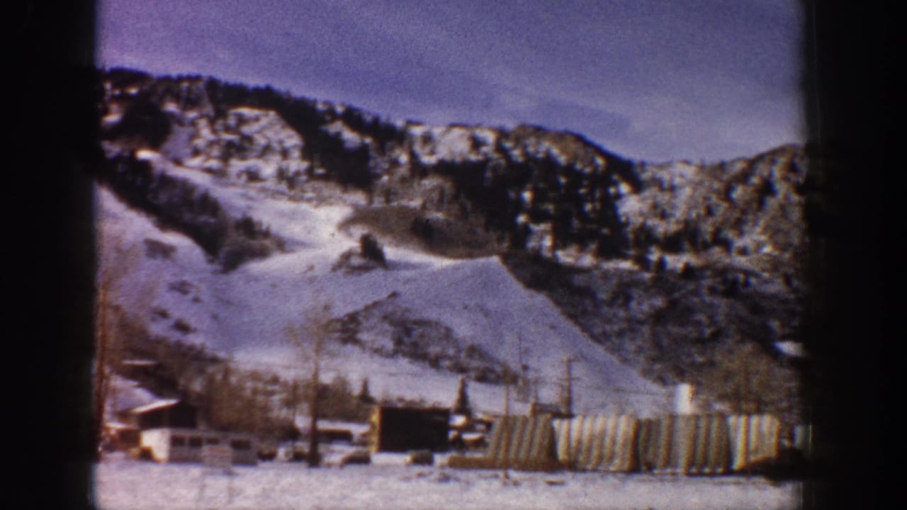 Wide 8mm home-movie shot of snow-covered mountain slopes and village buildings at base, consistent with early 1960s Aspen, Colorado.