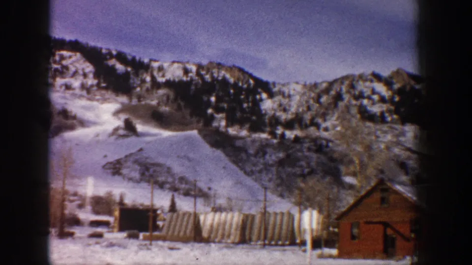 Slightly repositioned wide 8mm shot of snow-covered slopes and village base at what appears to be Aspen, Colorado, circa 1961, with a red timber building at right.