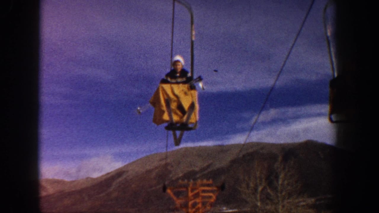 A rider in white winter hat ascends on a vintage single-seat chairlift with yellow cover at what appears to be a Colorado ski resort, circa 1961, filmed on 8mm.