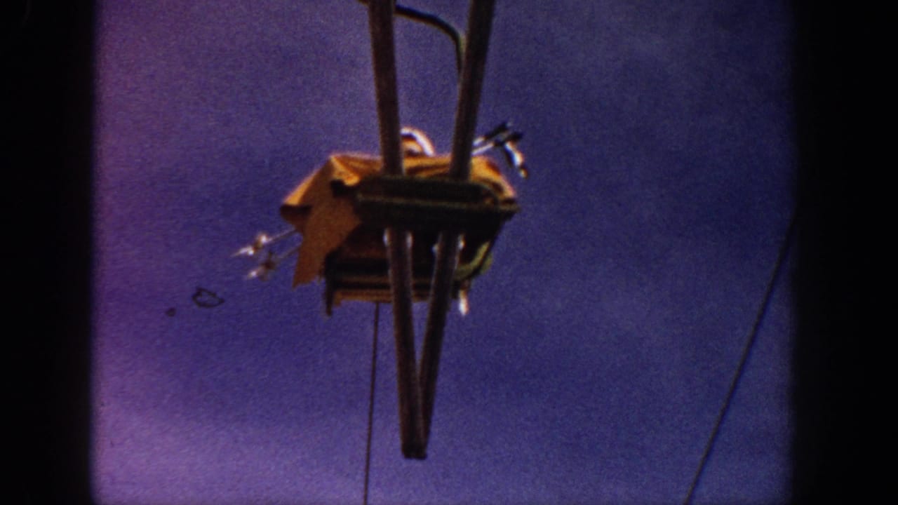 Close-up detail of a vintage single-seat ski lift grip assembly and cable hardware, yellow chair visible from below against a blue-purple sky, circa 1961.