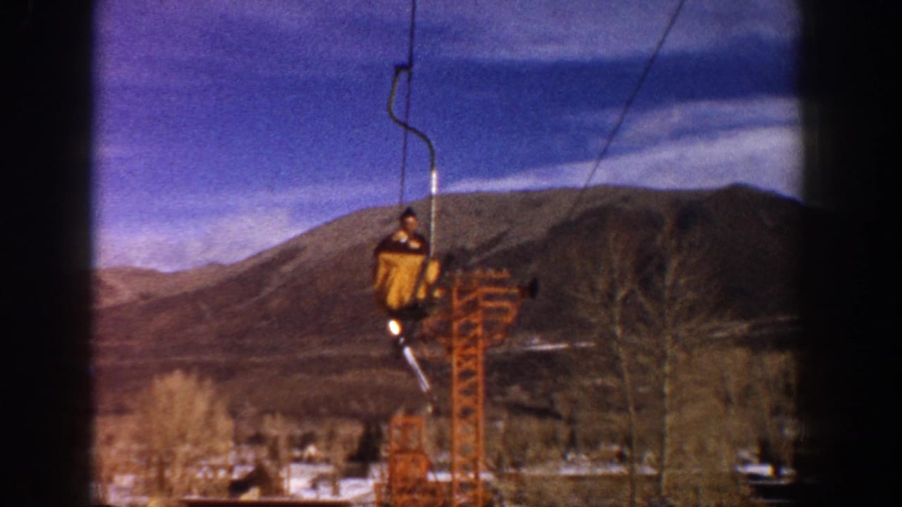 Man ascending ski lift at Aspen, Colorado, circa 1961; orange chairlift tower and snow-dusted mountains on 8mm color film.