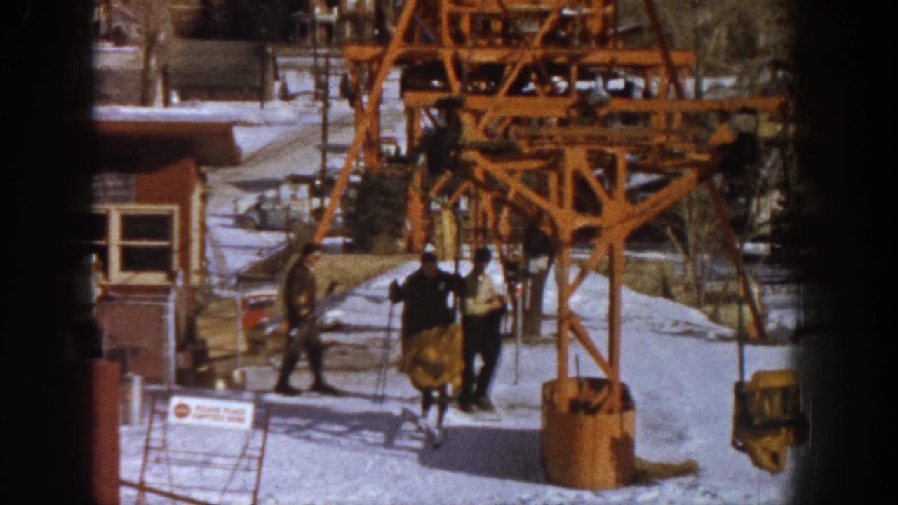 Early 1960s ski resort base at Aspen, Colorado, showing a large orange wooden lift tower and figures in heavy winter coats, captured on 8mm home movie film.
