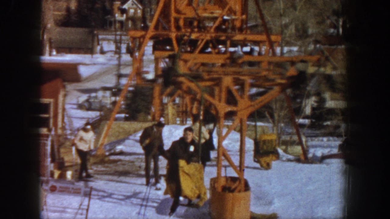 Final 8mm home movie frame showing candid activity near a wooden ski lift loading area, figures in period winter clothing, Aspen ski resort, Colorado, 1961.
