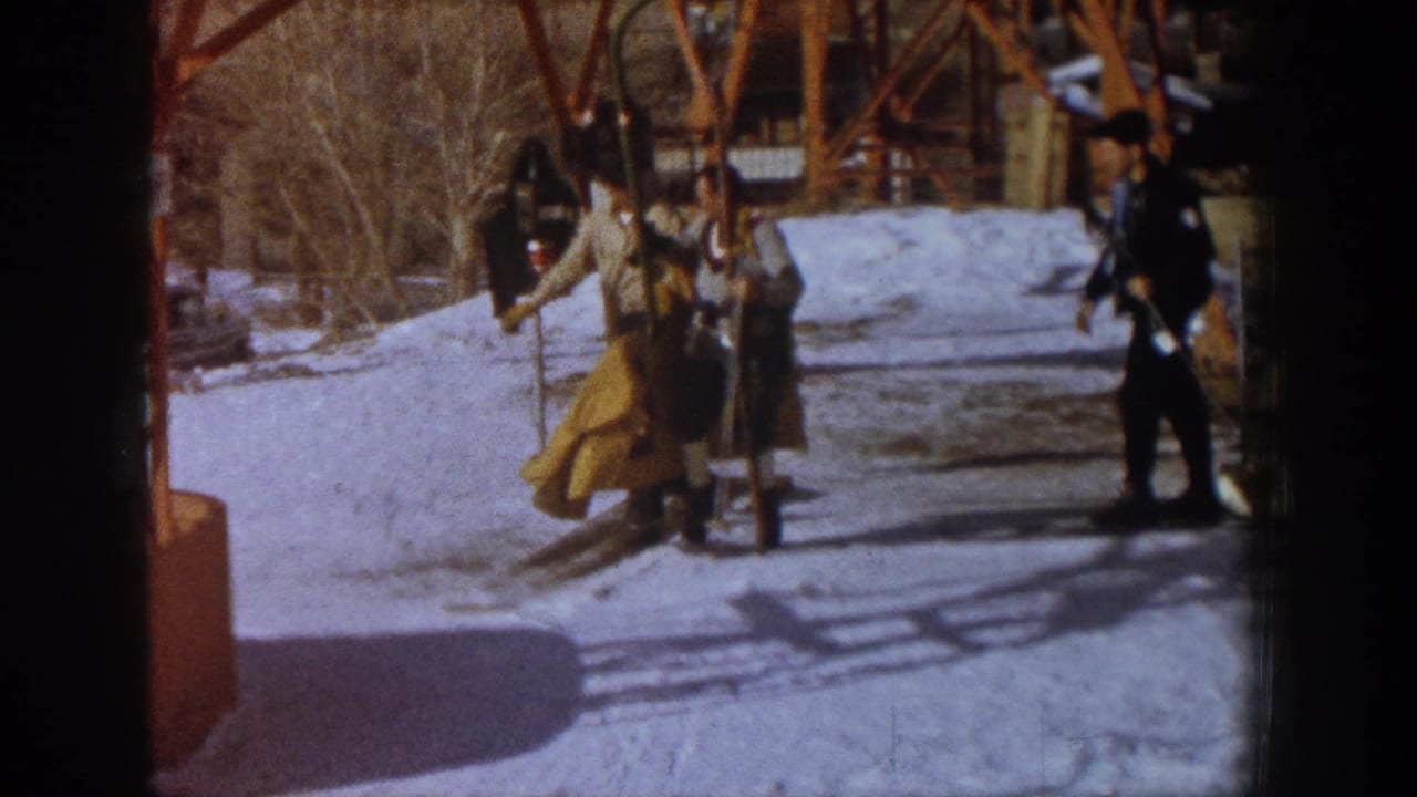 Group of adult skiers in early-1960s clothing at the base of an orange-framed ski lift, likely Aspen, Colorado, 1961; warm 8mm color cast with strong shadows