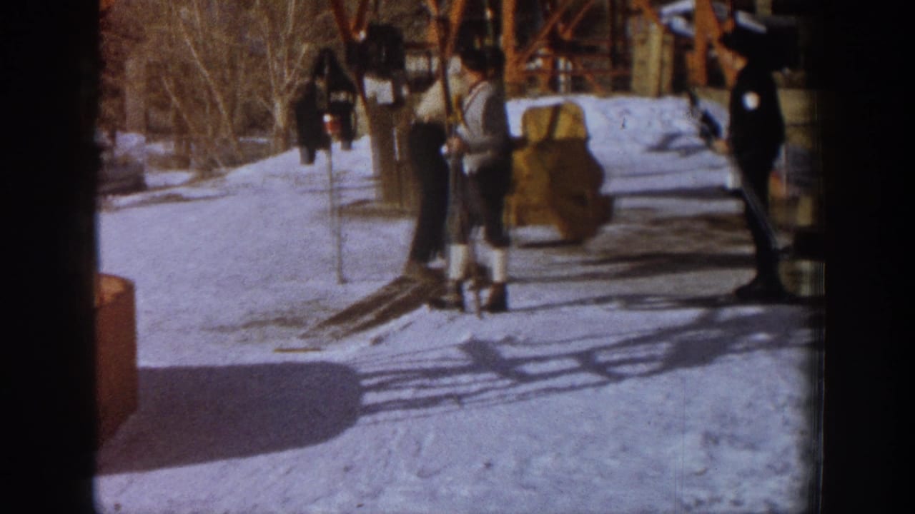 Several skiers stand near orange lift structures on packed snow, one in a patterned top visible in center