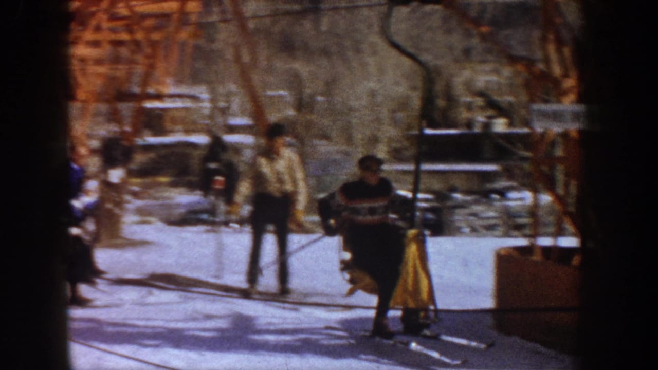 Wide view of skiers at a 1960s ski lift base, likely Aspen, Colorado; man in dark patterned sweater and yellow equipment visible at right in warm 8mm tones