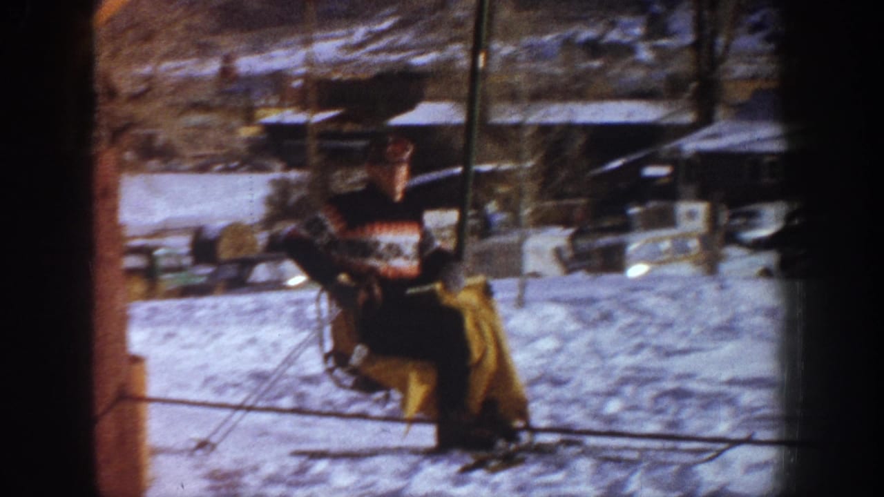 A skier in a patterned sweater and yellow pants rides a wooden chairlift at what metadata identifies as Aspen, Colorado, circa 1961, with period vehicles visible in the background.