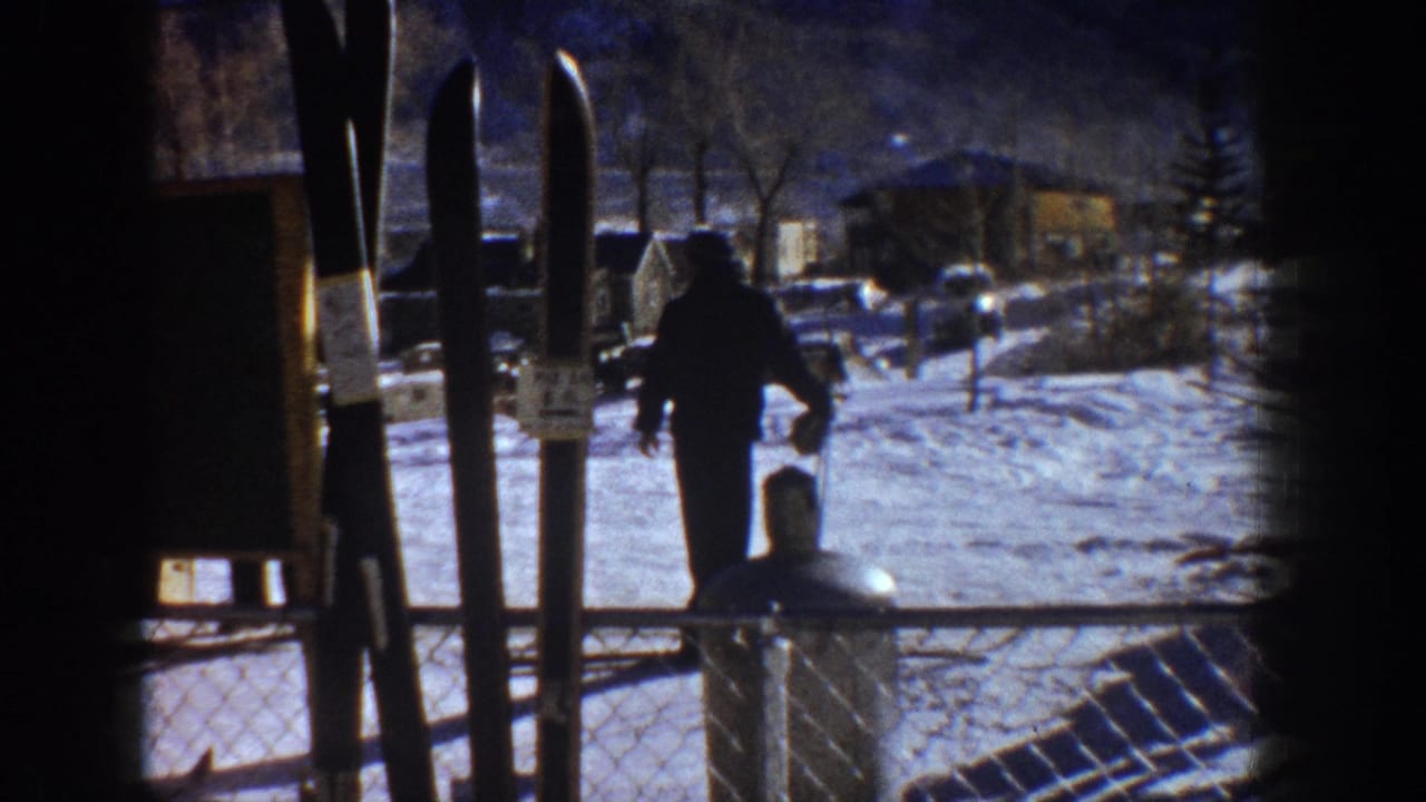 Ski area base, possibly Aspen circa 1961 — skis silhouetted in the foreground, a lone figure crossing toward low structures on snow-covered ground.