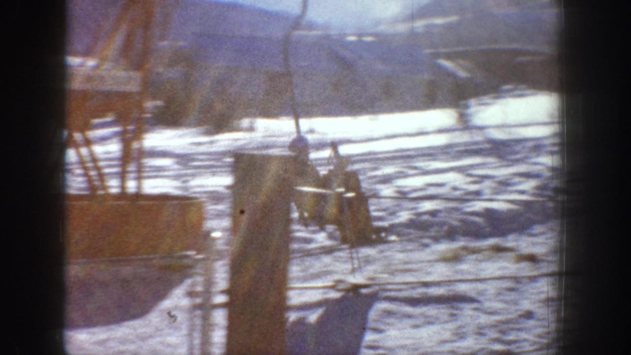 Ski lift cable and wooden support post in foreground with snow-covered slope behind, warm daylight tones.