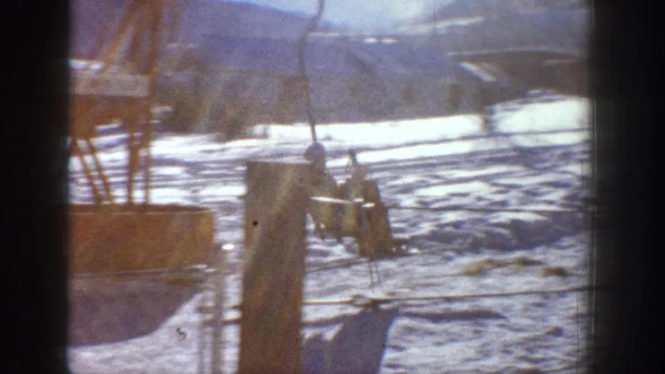 8mm home movie frame showing ski lift infrastructure and wooden post on a snowy slope, likely Aspen, Colorado, circa 1961.