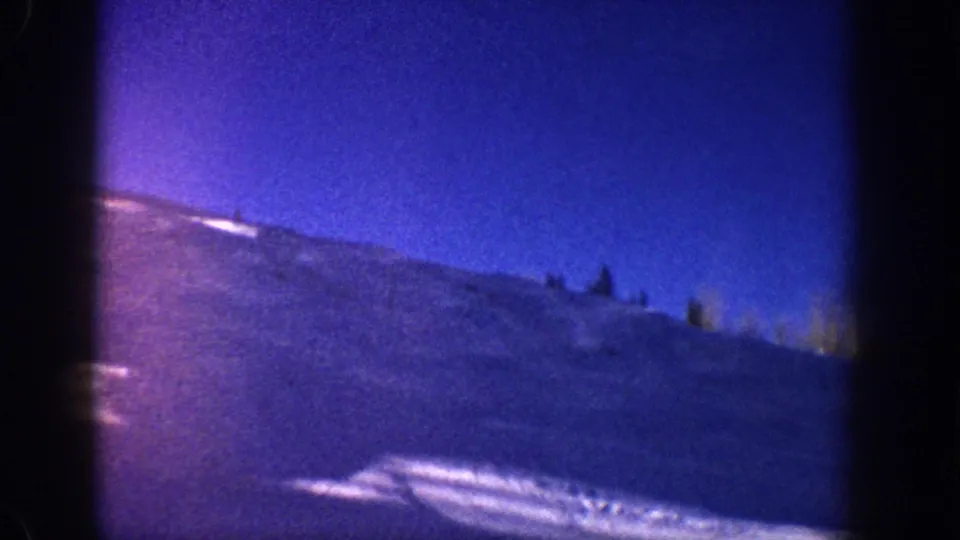 8mm panoramic alpine view with blue-purple color shift and silhouetted evergreens on ridgeline, likely Aspen-area mountains, circa 1961.