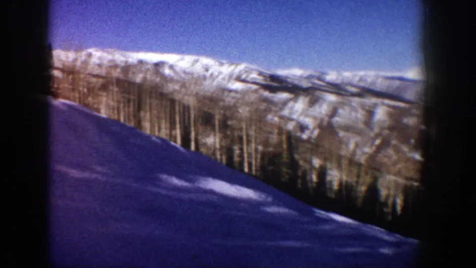 Final 8mm frame from Aspen, Colorado, circa 1961: snow foreground, prominent stand of bare aspens, lit distant mountain ridge under blue sky, with slight edge vignetting.