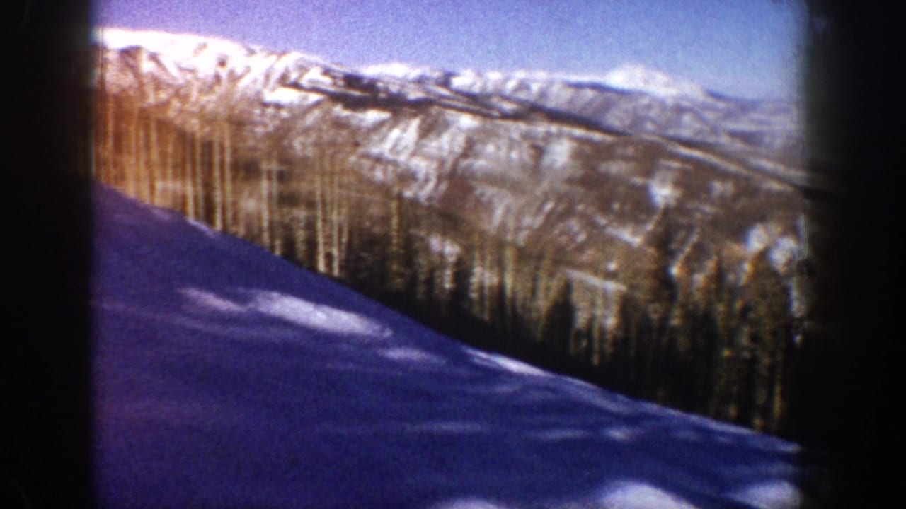 Foreground snow slope in deep blue-purple shadow with diagonal tree cast shadows, conifer belt, and ridgeline; Aspen, Colorado area, circa 1961, 8mm color film.