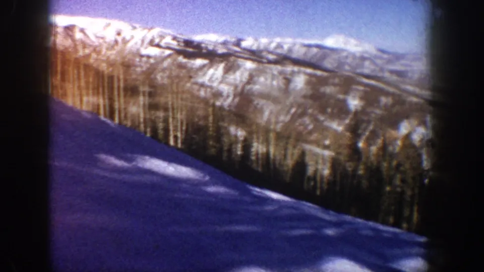 Foreground snow slope in deep blue-purple shadow with diagonal tree cast shadows, conifer belt, and ridgeline; Aspen, Colorado area, circa 1961, 8mm color film.