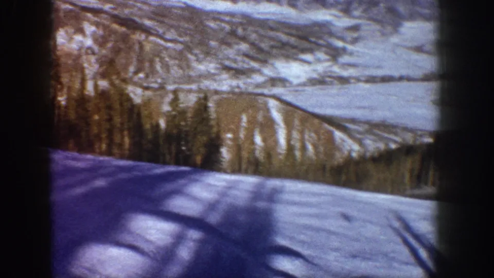 Pan opening onto a broad snowy mountain valley with shadowed foreground slope and layered ridges; Aspen, Colorado area, circa 1961, 8mm color footage.