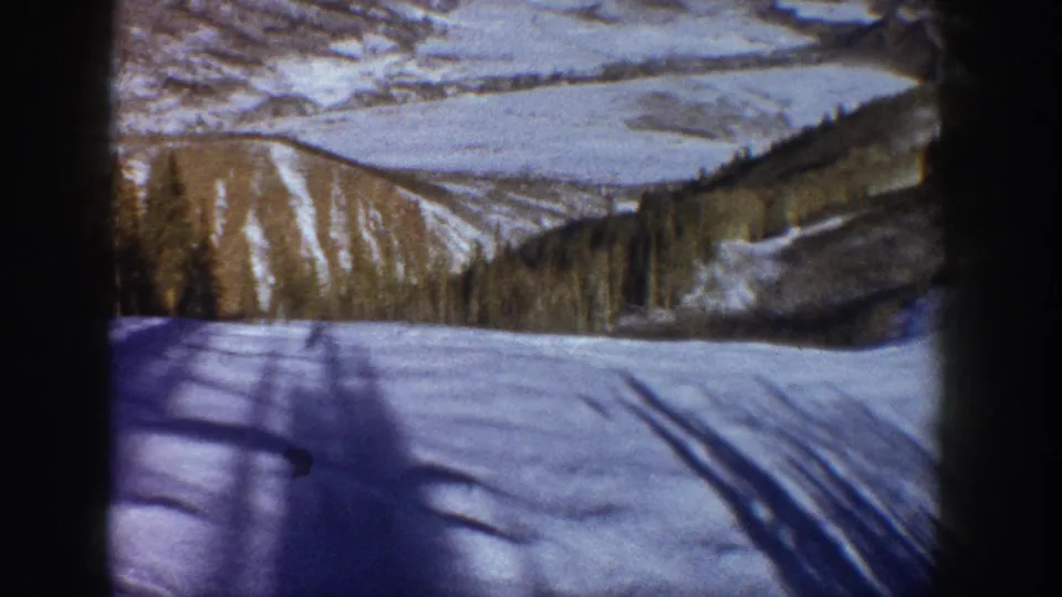 Final pan frame reveals a broad winter mountain valley, blue-shadowed foreground snow, conifer belt, and ridgeline; Aspen, Colorado area, circa 1961, 8mm home movie.