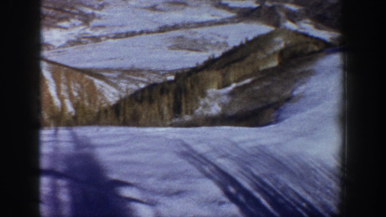 8mm home movie frame showing a snow-covered valley floor with diagonal shadow lines, forested ridge, and pale sky — Aspen, Colorado area, circa 1961.