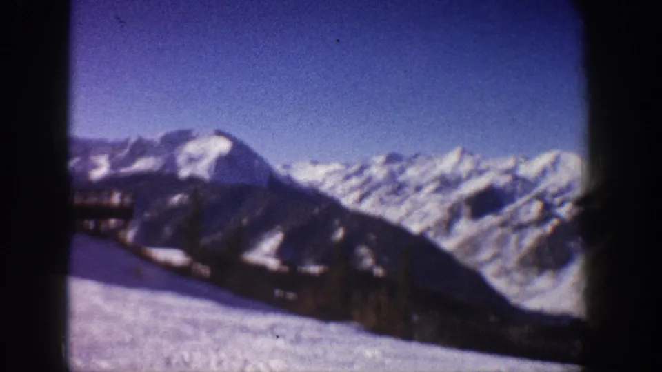 8mm frame circa 1961 of snow-covered Aspen-area mountains under clear blue sky, wooden structure partially in frame at left as camera pans.