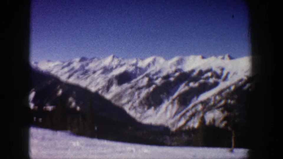 8mm frame circa 1961 capturing snow-covered Aspen-area mountain peaks with evergreen trees on lower slopes and pronounced film-edge vignetting.