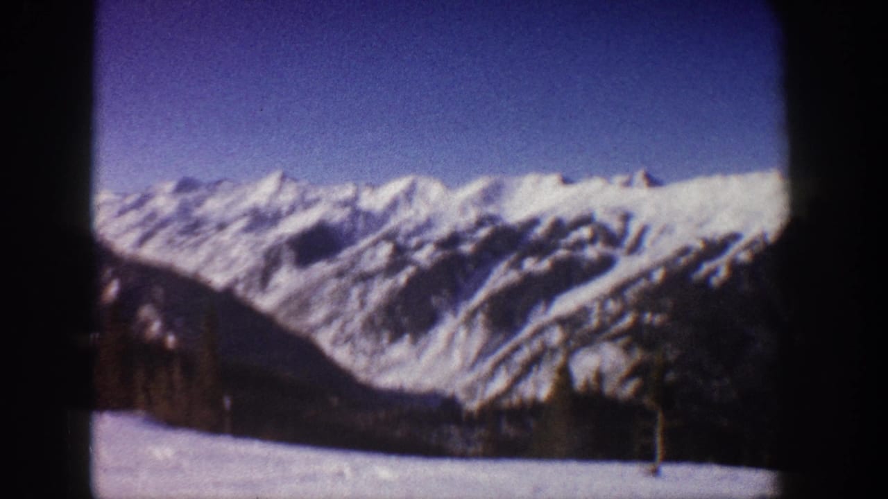 8mm home movie frame showing snow-covered Rocky Mountain peaks under a clear blue sky, Aspen, Colorado, circa 1961