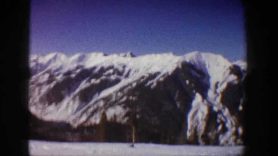 8mm home movie frame showing snow-laden conifers in the foreground against snow-covered Rocky Mountain peaks, Aspen area, Colorado, circa 1961