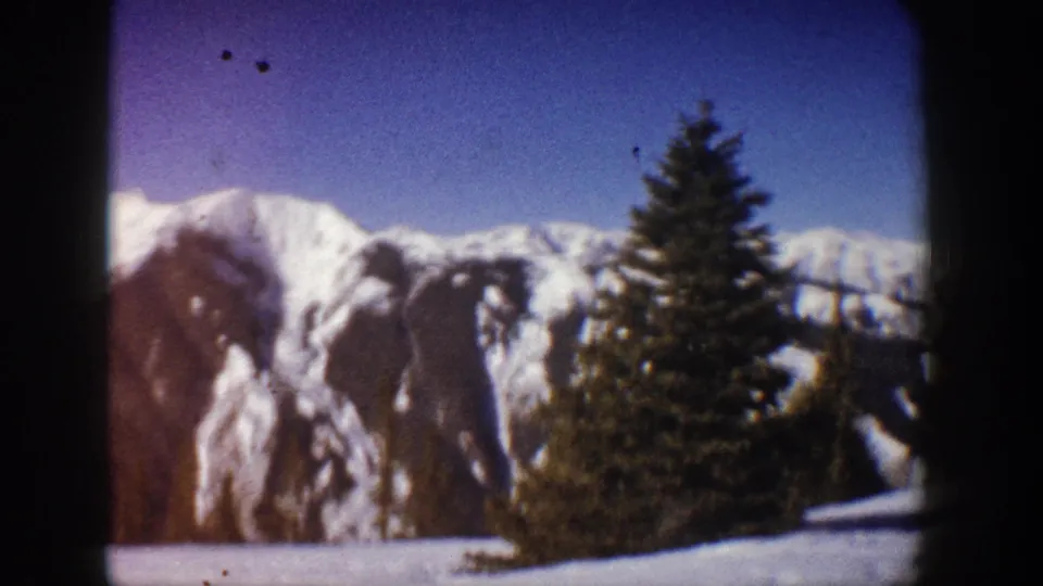 Mid-pan 8mm frame circa 1961 with a large spruce foregrounded against a snow-covered Colorado Rockies ridgeline, Aspen area.