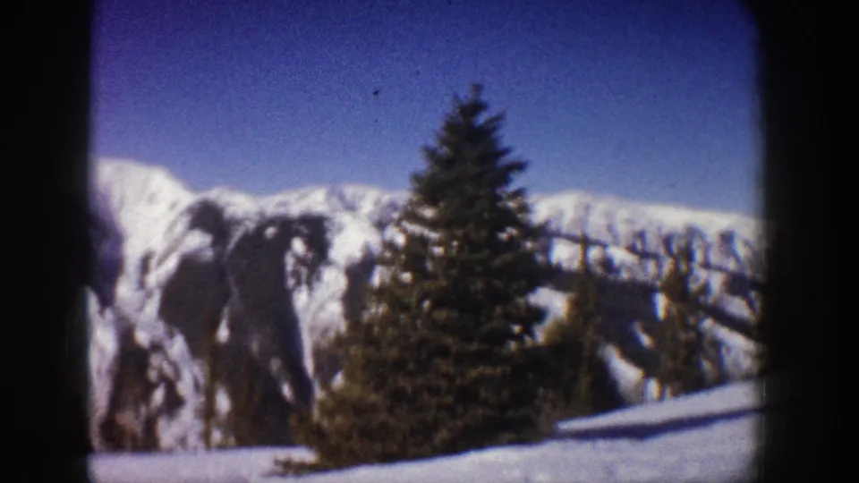 Final pan frame circa 1961 showing an evergreen tree and snow-covered Rocky Mountain ridgeline under blue sky, Aspen, Colorado area.