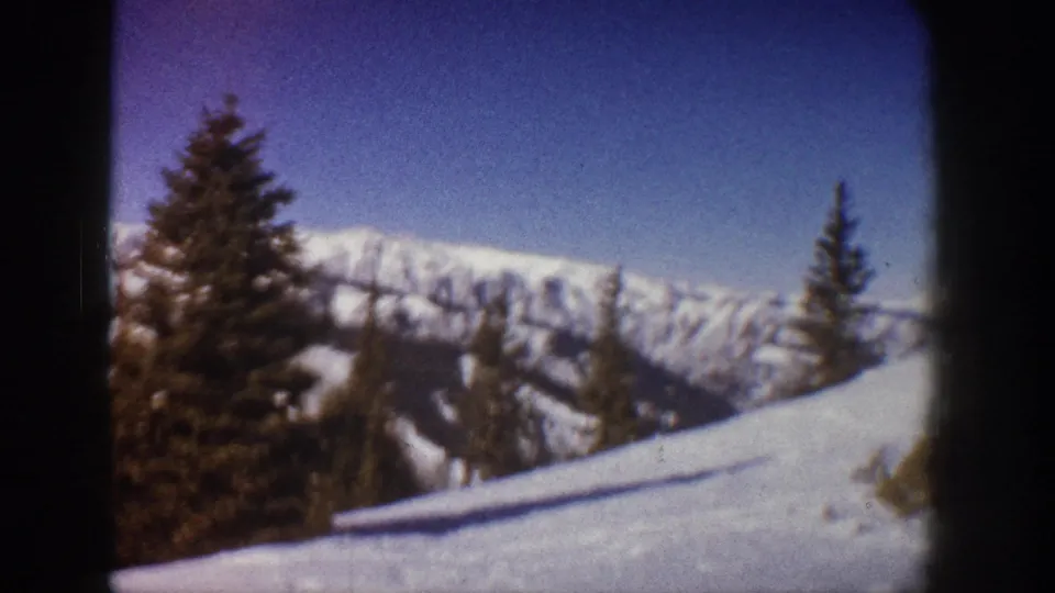 Later pan position in 8mm footage from what metadata identifies as Aspen, Colorado, 1961, showing a broad snow slope with scattered conifers and ridgeline.