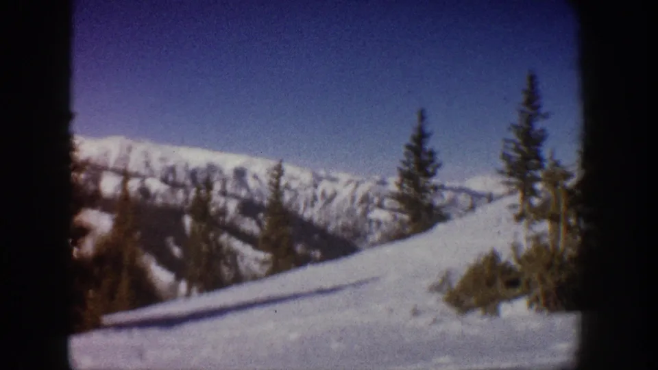 End-of-pan 8mm frame from 1961 Aspen, Colorado shoot showing scattered spruce trees across a snow slope under a clear blue sky.