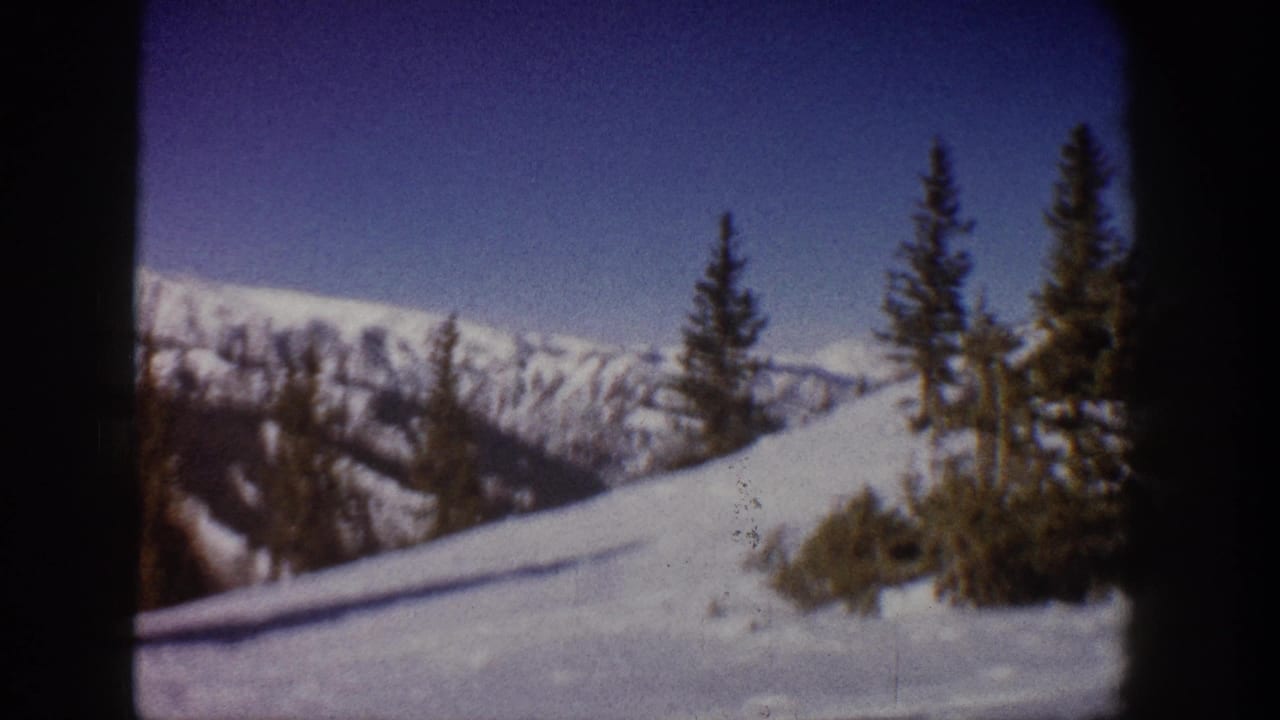 8mm home-movie frame circa 1961 of a sunlit ski slope at what metadata identifies as Aspen, Colorado, with conifers and a snow-covered mountain ridgeline.